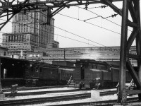 CNR boxcab electric 9103, originally Canadian Northern 603, sits at the head of a commuter consist at Montreal's Central Station while one of a kind "visibility cab" switcher CNR 7700 handles terminal switching duties.  Built in 1929 as the CNR's first diesel switcher locomotive, and powered with a 400hp Beardmore engine, CNR 7700 worked the Montreal area for a number of years, in addition to time at other terminals and on the <a href=https://www.railpictures.ca/?attachment_id=24039>Thousand Islands Railway.</a>  Renumbered to 77 in 1950, the  unit would be donated to Exporail in 1968.  Towering over the scene is the Sun Life Building, built in three phases from 1914 through 1933.<br><br><i>Original Photographer Unknown, Jacob Patterson Collection Negative.</i>