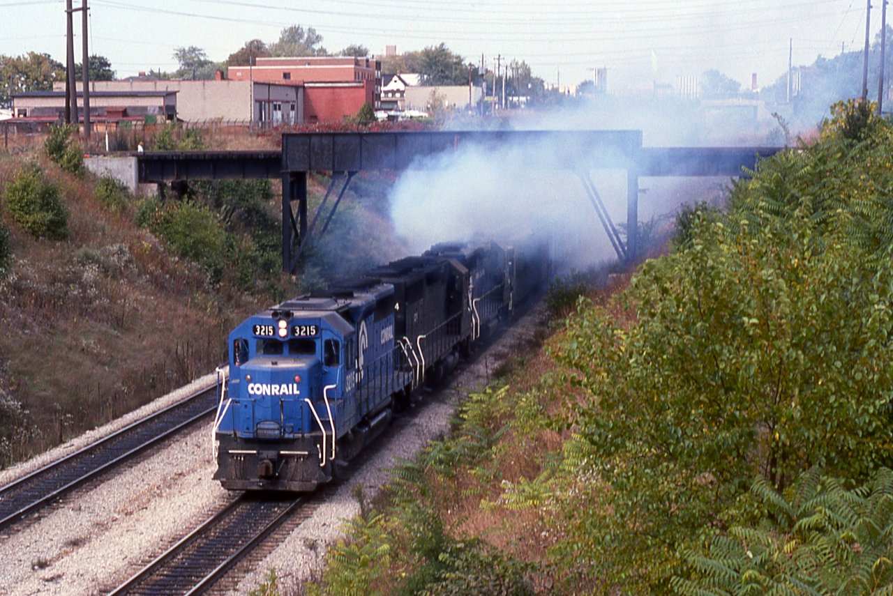 In a cloud of blue diesel exhaust, Conrail YDLN-2 appears to explode from the Detroit River Tunnel into Windsor, Ontario passing beneath the Essex Terminal Railway 'Black Bridge'.  The symbol YDLN means the job originated at Lincoln Yard (Y=Yard D=Detroit Div LN=Lincoln Yard)