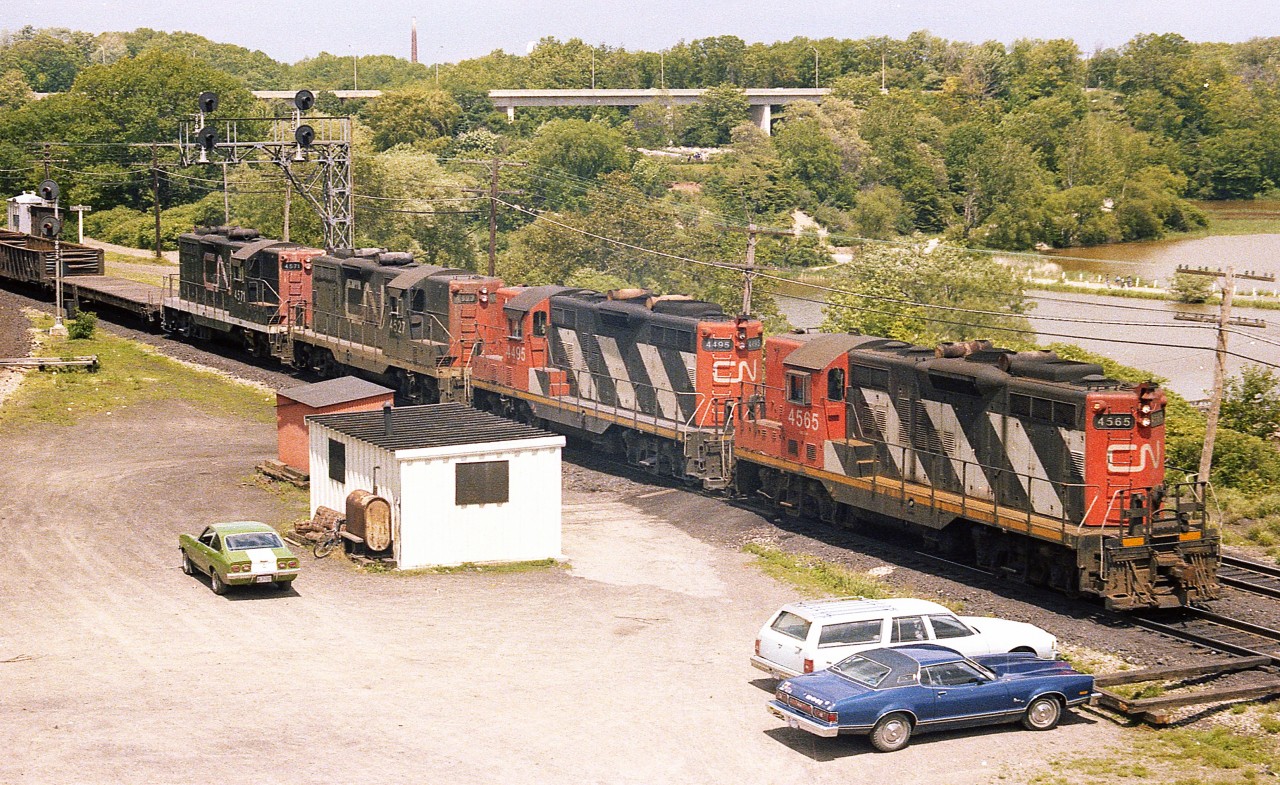 For me personally, this is a classic Bayview memory. A nice afternoon up on the hillside watching the Pulp train go by on its way Port Robinson and the setting out of many cars of logs for the Thorold Pulp and Paper company.
Yes, of course. All gone now as the GP9s have all been rebuilt, renumbered and or retired. And Thorold Paper has closed up shop.
Power this afternoon is CN 4565, 4495, 4527 and 4571. 
Don't know who owned that little Vega. My car is parked next to (the late) Bill McArthur's station wagon. I miss those days, and miss Bill a lot too.