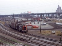 Downtown Toronto wasn't all passenger power and coachyards: CN SW9 7001 switches covered hoppers just east of Bathurst Street bridge (<a href=http://www.railpictures.ca/?attachment_id=48869><b>Cabin D interlocking</b></a>), in a view looking south to the Gardiner Expressway and harbourfront area (today, this is all condos). 
<br><br>
The white building is CN's Yard office, the train is on the lead that curved south under the Gardiner and lead to the Central Harbour District and Queen's Quay harbourfront trackage, including Loblaws (part of their warehouse on the right) and the Canada Malting grain elevator (further back). Piggyback flats, boxcars and cylindrical covered hoppers pack the team tracks, storage tracks, piggyback ramps, and Cottrell Forwarding freight LCL platforms scattered here.
<br><br>
The lead on the right curving past Loblaws (note crossbucks) connects to the CP ex-TG&B Wharf Leaf that ducked out of view under Bathurst Street, passed through CP's Fez City Yard, under the Gardiner past Molson's, across the Oakville Sub at Cabin E interlocking, and on to the Liberty Village and Parkdale Yard areas (this was CP's western access to the downtown harbourfront industrial trackage).
<br><br>
On the left, tracks lead to Union Station, CN Spadina Roundhouse/Coachyard, and the "high line" mainline freight bypass.
<br><br>
<i>Original photographer unknown, Dan Dell'Unto collection slide.</i>