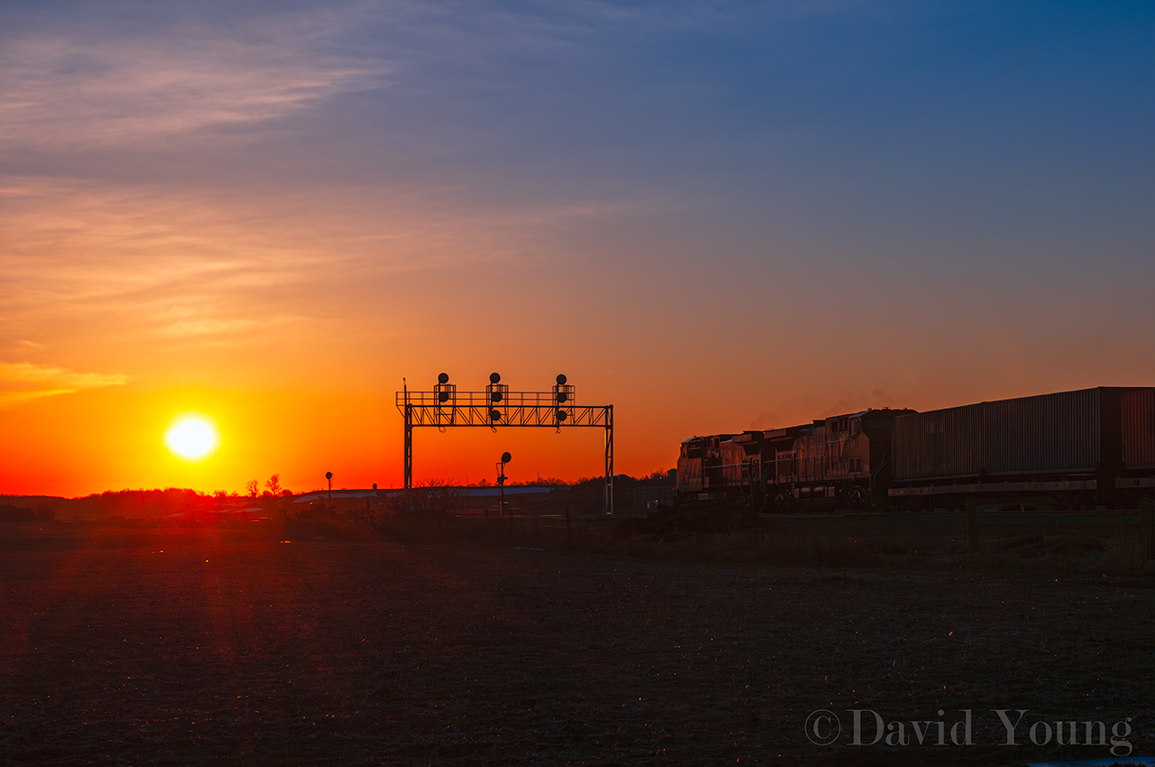 The Evening Wolverton Came Online. The sun sets over the fields west of Cambridge as train 159-27 enters the new siding at Wolverton. The old ABS signals still stand beneath the new signal bridge, turned away and out of service, their purpose now redundant. The original siding will remain as a future storage track for the yard that will built here in the coming years. 159 will be the first of 3 westbounds block-on-block (Ham Turn and 243) to squeeze into the new 10,000 foot siding to meet 5 eastbounds.