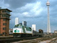 Coal towers, control towers, office towers and CN towers: GO Transit F40PH 512 trails on an inbound Toronto commuter train just east of Cabin D interlocking near Bathurst Street bridge, passing CN S13 8518 running light power between switching duties at Spadina Coachyard. On the left is one of the CN yard towers in the area (there was one here, another at Don Yard, one in Mimico Yard and another at Mimico near Canpa), on the right are leads to the coachyard and the coaling towers in the distance, near Spadina Roundhouse. The new CN Tower (completed three years earlier) looms taller than any of the downtown office buildings.<br><br>In a few years this area would undergo massive changes as a flyunder was dug right here in the early 80's, the old Cabin D tower and interlocking plant automated (as Bathurst Street), the CN Bathurst freight yard (to the left) rebuilt for storing GO Trains, and not long after VIA would close its former CN Spadina diesel and passenger servicing facilities in 1985 in favour of moving them to Mimico.<br><br><i>Original photographer unknown, Dan Dell'Unto collection slide.</i>