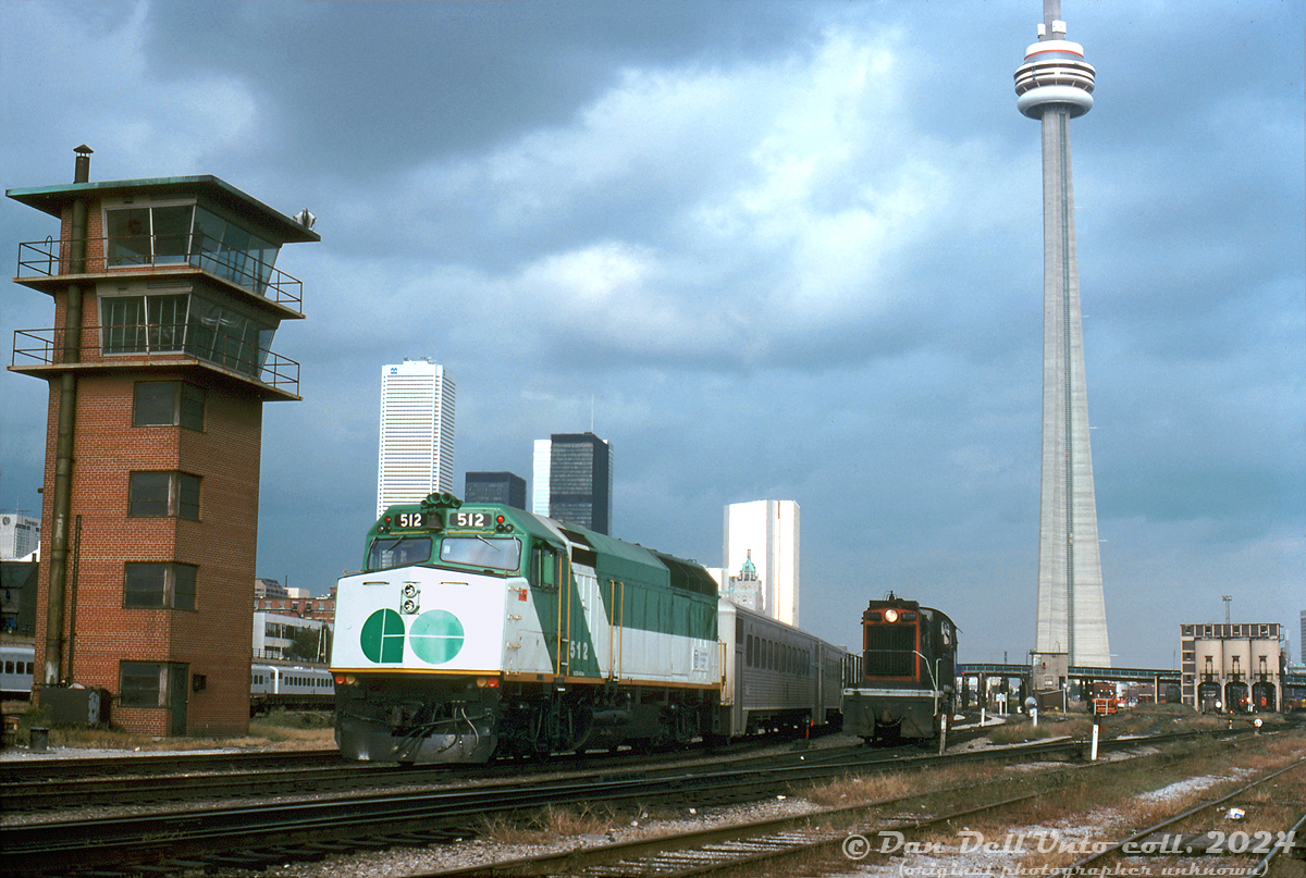 GO Transit F40PH 512 trails on an inbound Toronto commuter train just east of Cabin D interlocking near Bathurst Street bridge, passing CN S13 8518 running light power between switching duties at Spadina Coachyard. On the left is one of the CN yard towers in the area (there was one here, another at Don Yard, one in Mimico Yard and another at Mimico near Canpa), on the right in the distance are the coaling towers near Spadina Roundhouse.

In a few years this area would undergo massive changes as a flyunder was dug right here in the early 80's, the old Cabin D tower and interlocking plant automated (as Bathurst Street), the CN Bathurst freight yard (to the left) rebuilt for storing GO Trains, and not long after VIA would close its former CN Spadina diesel and passenger servicing facilities in 1985 in favour of moving them to Mimico.

Original photographer unknown, Dan Dell'Unto collection slide.