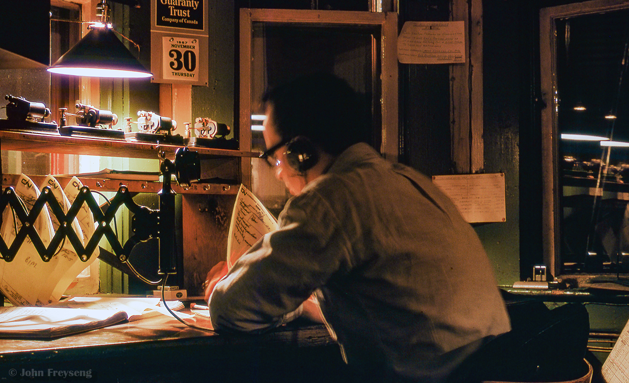 CPR train order operator John F. Mellow is seen at work, copying out orders at Don Station on a chilly winter night.  Employed by the CPR as an operator/dispatcher for 15 years, and later 29 years with GO Transit, John was heavily involved for many years with the Upper Canada Railway Society, Ontario Rail Association, South Simcoe Railway, the Friends of Freeman Station in Burlington, Toronto Railway Museum, and various other rail preservation projects.

"Every time I see a picture of Don Station, I think of my dear friend John. Can hear him repeating the train order he is writing down, spelling out numbers, hunched over the train order sheet, in the quiet of the night. This is how I like to remember John, and I feel blessed to have shared many wonderful and enjoyable times with him throughout his remarkable life."  1945 - 2025.

>Scan and editing by Jacob Patterson.