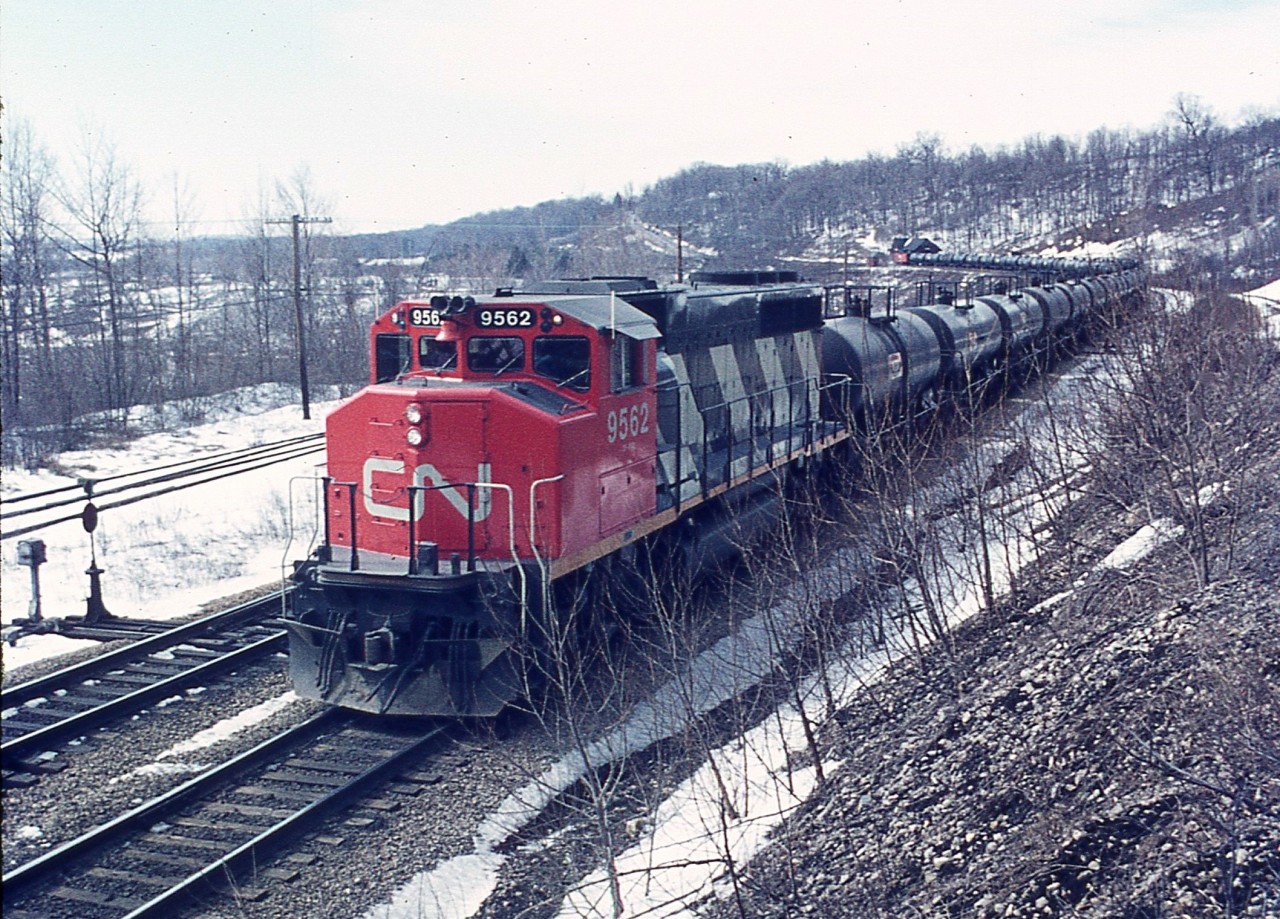 One of those days in which I was getting impatient for spring time, I guess. Was wandering up the old incline to the Canada Crushed Stone facility when I happened to notice an eastbound train in the distance. Oil train? In the distance the old Dunas station can be seen, along with the caboose on the rear. CN 9562 sole power. On the extreme right is the incline track I am walking along; and on the left is the track that ran off the main line down into Steetleys (Canada Crushed Stone) quarry operations. Operations ceased in the 1970s; track pulled up and the area below the tracks in now a housing development.