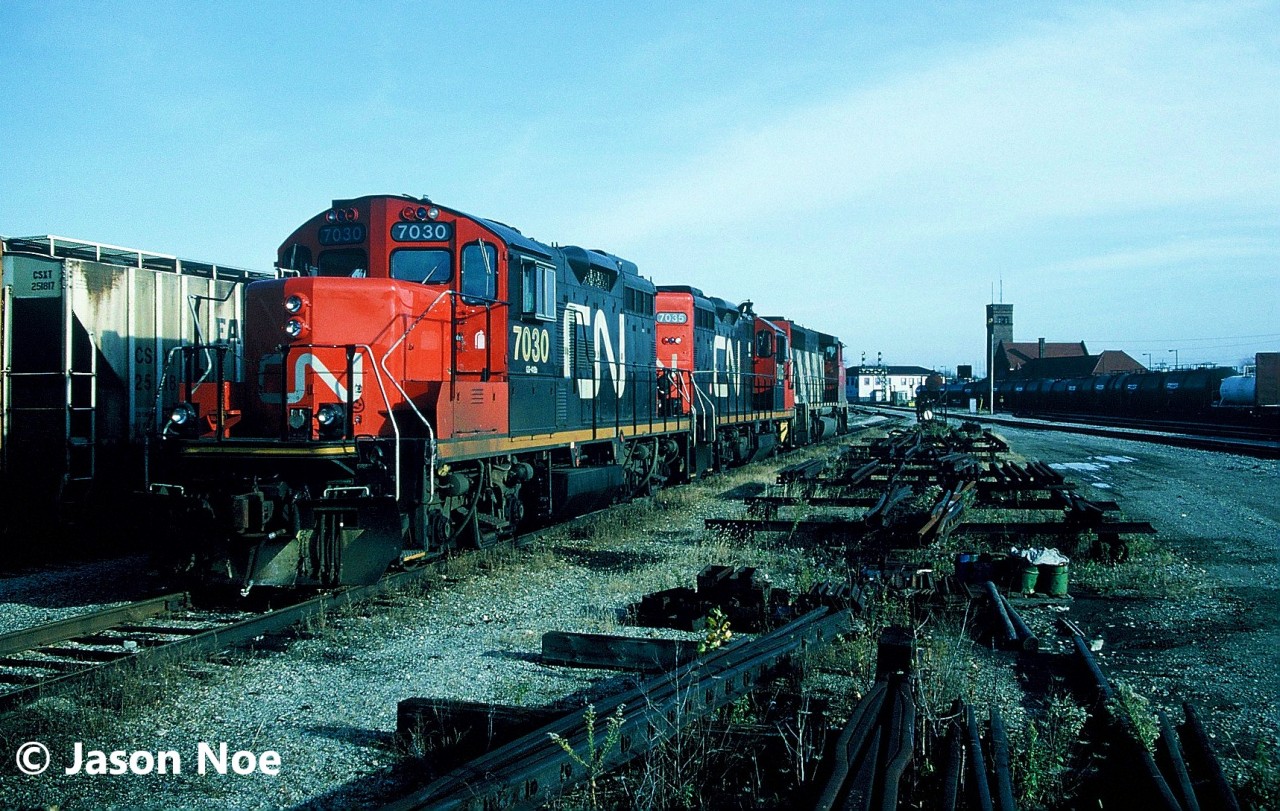 CN power is viewed idling in the Brantford, Ontario yard over the weekend with the station in the background. It includes; GP9RM’s 7030 and 7035 as well as GP40-2L(W) 9458. At the time, the Burford Spur was still active to Burford and all of Brantford’s active rail customers were serviced from this yard.