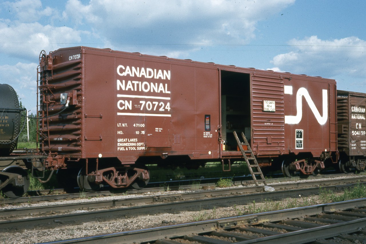Another rebuild for OCS  
Further to the Generator Clothes Drying Car pic I posted a few days ago ( http://www.railpictures.ca/?attachment_id=58278 ), here is another 40' revenue boxcar converted to OCS duties. 
CN 70724 is a Great Lakes Region Engineering Department Fuel & Tool Supply Car pictured here in the consist of GLR Tie Gang #4 at Oba, ON in July 1976. 
This car was rebuilt along with many others in a project at Pointe St. Charles shops in Montreal during October 1975 (H.Q. 10 .75) 
Some interesting features on this car are: 
-high brake wheel and foot stand 
-no roof running boards 
-ladder rails left in place, but higher rungs removed (at far end of car) 
-lower foot stand added to aid in refueling the 1000-gallon reservoir inside the car 
-coupler painted in error (AAR Rule 18) 
-consolidated stencil under CN logo at far end 
-ACI (Automatic Car Identification)/Kar Trak label (left of door opening)