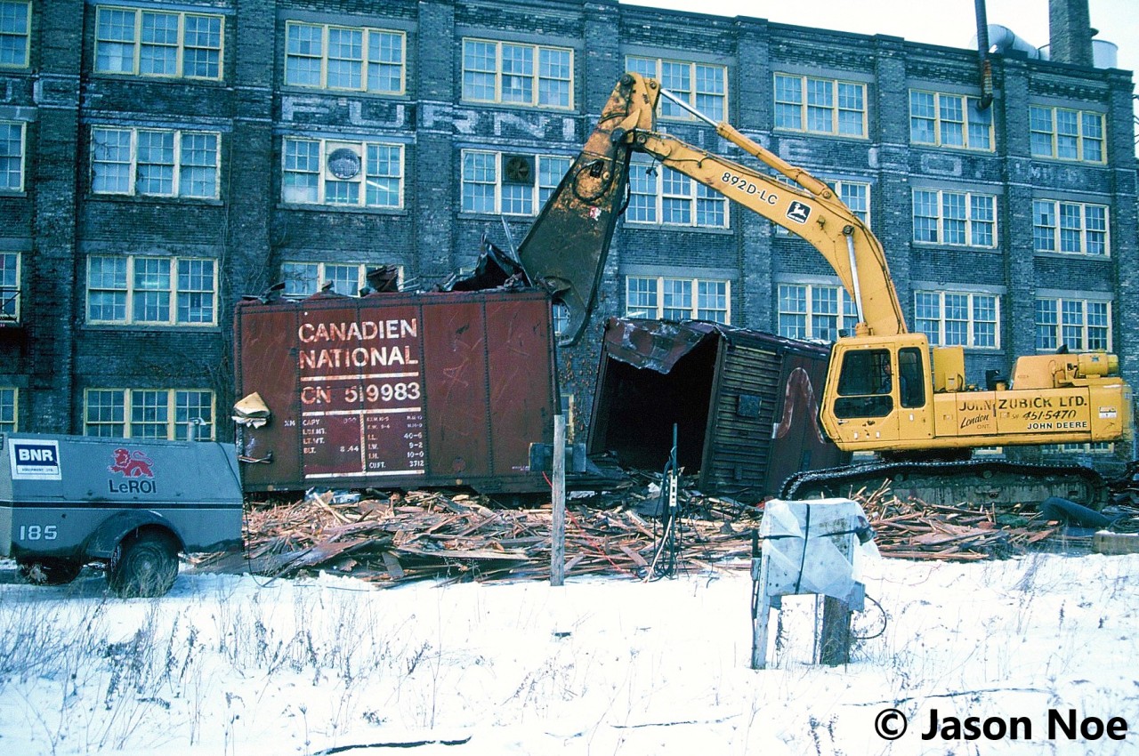 I remember coming home from school and getting a phone call from a friend saying that I needed to get down to the station immediately. My first thought was that there were possibly some CN detours over the Guelph Subdivision, however he informed me that the old CN boxcars across from the station were being prepared to be scrapped on site that afternoon. 

A short drive later and the scene was as expected, with big equipment from London-based John Zubick making quick work of each boxcar. For as long as I was a kid, those boxcars had been a part of the railway scene in Kitchener and were used as storage by local CN maintenance of way workers and carmen. While taking in the scene as each boxcar was systematically sheared open by the equipment and turned into pieces, one such memory comes to mind. As the excavator dug deep into one of the boxcars it removed an almost pristine wooden CNR railway crossing sign still attached to its post that had been long stored inside. Within seconds…chomp, chomp chomp. Even after three decades, remembering that still stings a little. 

Here, CN 519983 meets its fate across from the Kitchener station. While this one had the CN noodle, several of the other boxcars scrapped that day had their original CN maple leaf logos.