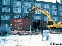 I remember coming home from school and getting a phone call from a friend saying that I needed to get down to the station immediately. My first thought was that there were possibly some CN detours over the Guelph Subdivision, however he informed me that the old CN boxcars across from the station were being prepared to be scrapped on site that afternoon. 
<br>
A short drive later and the scene was as expected, with big equipment from London-based John Zubick making quick work of each boxcar. For as long as I was a kid, those boxcars had been a part of the railway scene in Kitchener and were used as storage by local CN maintenance of way workers and carmen. While taking in the scene as each boxcar was systematically sheared open by the equipment and turned into pieces, one such memory comes to mind. As the excavator dug deep into one of the boxcars it removed an almost pristine wooden CNR railway crossing sign still attached to its post that had been long stored inside. Within seconds…chomp, chomp chomp. Even after three decades, remembering that still stings a little. 
<br>
Here, CN 519983 meets its fate across from the Kitchener station. While this one had the CN noodle, several of the other boxcars scrapped that day had their original CN maple leaf logos.
