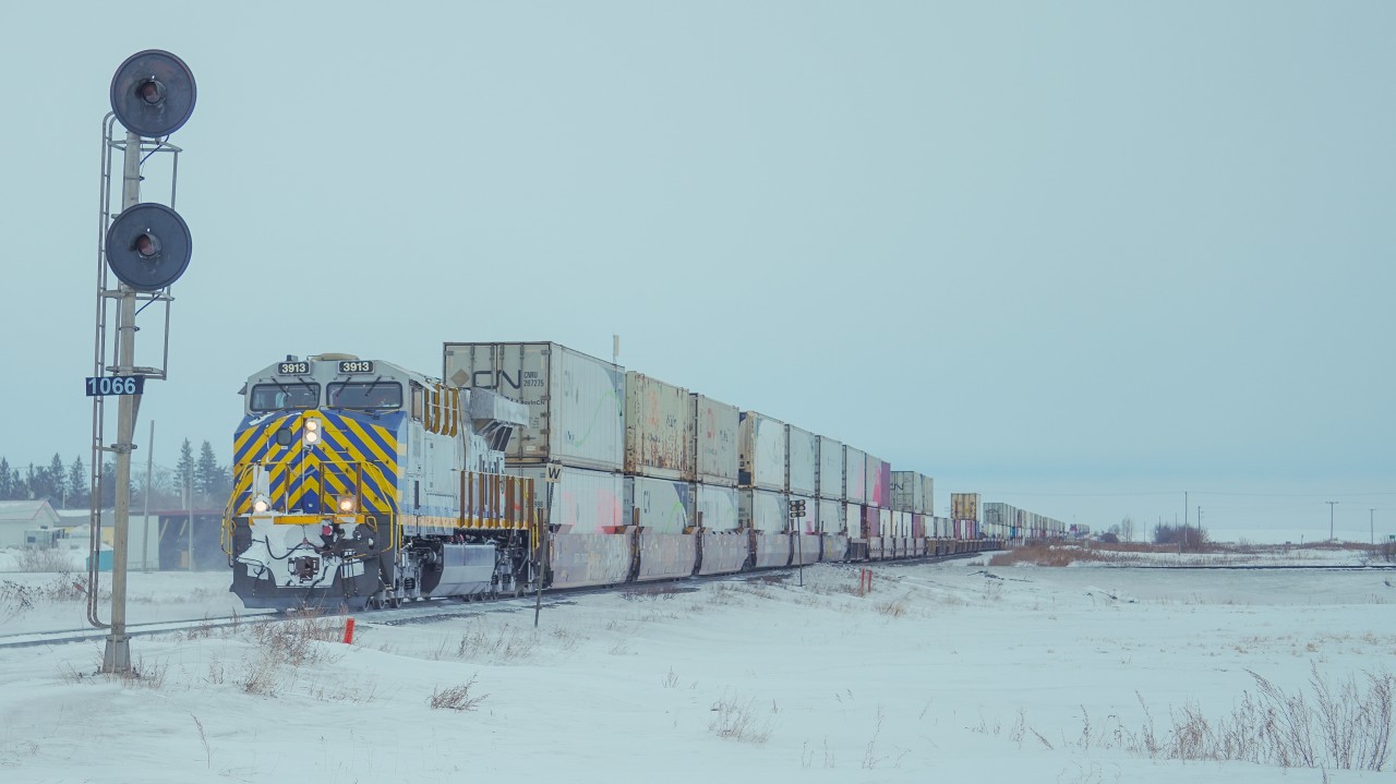 A CN intermodal led by CN 3913 crosses the diamond at Nokomis Saskatchewan where the Canadian National's Watrous Subdivision and Canadian Pacific Kansas City's Lanigan Subdivision cross each other. Seen is this photo is a remaining searchlight, which are now slowly disappearing amongst many modern subdivisions.