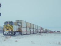A CN intermodal led by CN 3913 crosses the diamond at Nokomis Saskatchewan where the Canadian National's Watrous Subdivision and Canadian Pacific Kansas City's Lanigan Subdivision cross each other. Seen is this photo is a remaining searchlight, which are now slowly disappearing amongst many modern subdivisions.