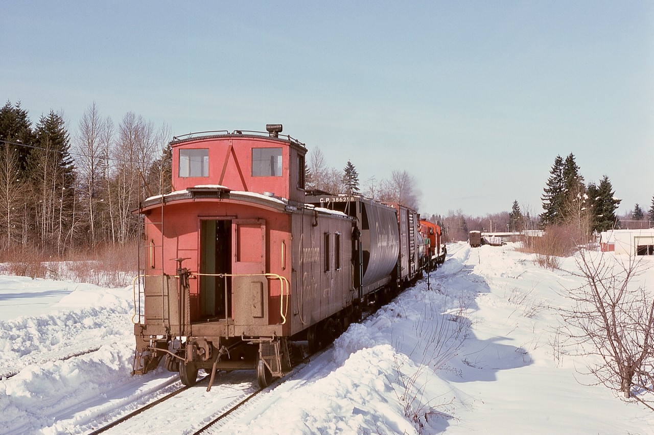Twice-weekly (Tuesday and Friday) freight train No. 65 from Wellcox yard in Nanaimo has just arrived Courtenay with back-to-back Baldwins CP 8001 and 8010 and caboose CP 437030 (with marker lamps already positioned for the return trip) on Friday 1975-02-14 and is preparing to switch its train.  On the left, snow outlines where a wye had been until removed a few years ago.  With no timetable schedule for southward freight trains, the return to Wellcox will be as an Extra.
