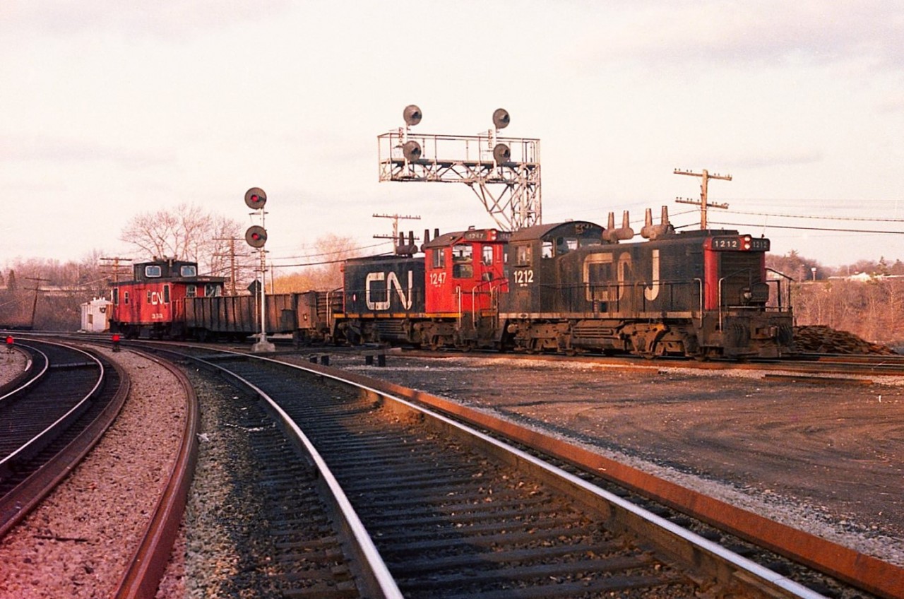 One thing that made Bayview so interesting for so many of us back in the day was the endless activity of the little GMD  SW switchers of various models that made the rounds daily; whether little runs into Aldershot from Hamilton and return or perhaps wyeing the pigs in order to load them properly down at the Stuart St facility. Add in the VIAs and mainline freights and it seemed there was always something going on.
This image is of a typical transfer.  CN 1212 and 1247 with van #79474 returning to Hamilton with but a single gon. By the looks of the sun angle, this was a rather late day shot. But still, it was something, and that something is now history.
CN 1212 retired in 1989, and the 1247 in 1995.