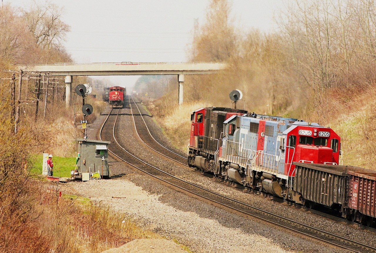 Copetown memories:
The original track was laid thru here back in the 1850s by the Grand Trunk. Problems developed in this stretch of track between mile 9.0 and 9.1 Dundas sub after a second track was put in. Apparently the underlying ground was of a sandy silt nature and ground water seeping in caused some instability in the track bed. Problems grew worse as trains became more frequent, longer and heavier. Water was at times pooling between the rails.  By 1995 a slow order restricted trains to 5 MPH over this stretch and a watchman was on duty 24 hours a day who kept an eye on the railbed as each train rolled over. CN shored up and realigned the track frequently. Beginning around 2013 and completed not long after, the railroad using new technology put a hopefully permanent end to the problem, and the slow order lifted and watchman removed.
In this photo, eastbound, coming at the photographer is #386 with CN 9489, CR 6479, CN 7106 and 4132. Heading west is #387 powered by CN 5626, GT 6413 and 6205.
Off to the left by his "shanty" stands the watchman. Note he has some conveniences, such as his lawn chair so he can sit out and catch some rays.  I wonder if he cut his own patch of lawn, too?
Not that many winters ago, maybe 2020, I walked the access laneway that led to the long gone shanty, and despite it was well below freezing, water was bubbling out of the hillside and running down thru the gravel.
The problem, in a minor way, still persists.