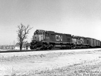 On a sunny October day in 1972, CN M636 2334 and SD40 5075 lead an extra freight off the Halton Sub at Burlington, about to enter the Oakville Sub and head west. The first few cars are passing over the Brant Street underpass.<br><br>This photo was taken not too long after the Brant Street grade separation project (that took place in the late 1960's). Looking at 1965 and present-day aerial imagery it's hard to note the exact changes, but it appears Brant Street was realigned to the east, and the (closer) houses in the background were once along the south side of Plains Road East where Burlington Hyundai is today. The Sunoco may be the same one on the SW corner that was a Petro Canada until recently. Some more gas pumps appear on the NE corner, and beyond that housing along Leighland Rd (visible before the current plaza was built).<br><br><i>Bill Grandin photo, Dan Dell'Unto collection negative.</i>