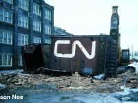 I remember coming home from school and getting a phone call from a friend saying that I needed to get down to the station immediately. My first thought was that there were possibly some CN detours over the Guelph Subdivision, however he informed me that the old CN boxcars across from the station were being prepared to be scrapped on site that afternoon.
A short drive later and the scene was as expected, with big equipment from London-based John Zubick making quick work of each boxcar. For as long as I was a kid, those boxcars had been a part of the railway scene in Kitchener and were used as storage by local CN maintenance of way workers and carmen. While taking in the scene as each boxcar was systematically sheared open by the equipment and turned into pieces, one such memory comes to mind. As the excavator dug deep into one of the boxcars it removed an almost pristine wooden CNR railway crossing sign still attached to its post that had been long stored inside. Within seconds…chomp, chomp chomp. Even after three decades, remembering that still stings a little.
Here, CN 519983 meets its fate across from the Kitchener station. While this one had the CN noodle, several of the other boxcars scrapped that day had their original CN maple leaf logos.
