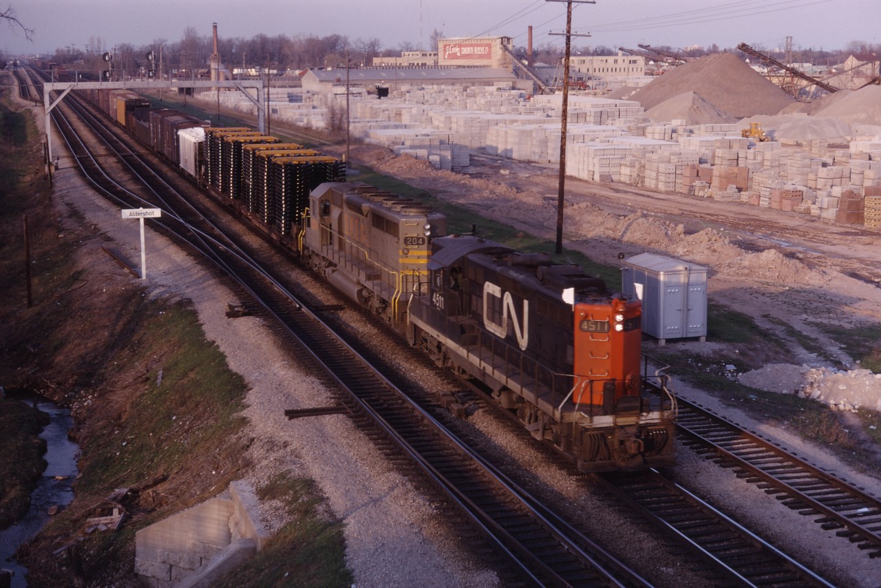 CN GP9 4511 and QNSL SD40 204 roll past the future site of the Aldershot GO station on a nice spring evening in 1969. As you can see, the lot used to be occupied by the large J Cooke Concrete Blocks business with a small CN yard (built in the 1960s) opposite.