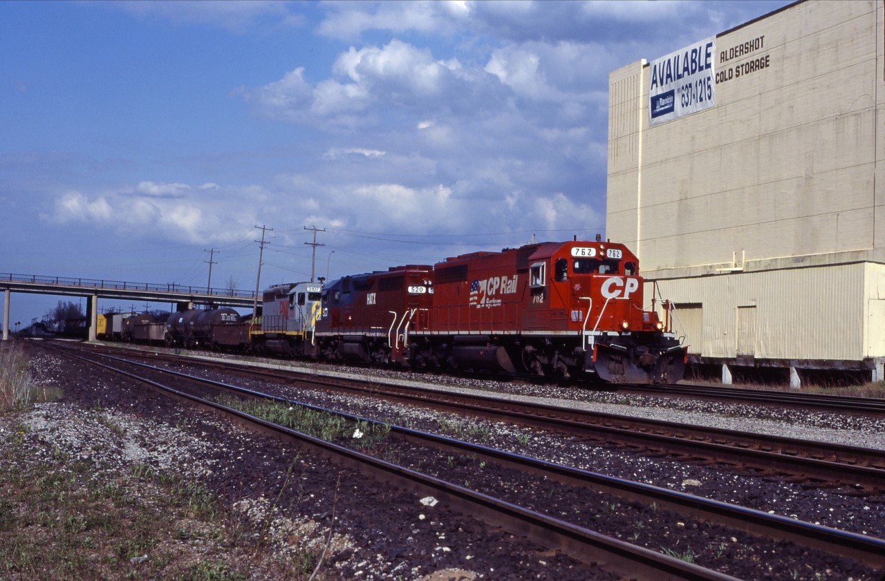 A CP westbound rolls past the Cold Storage building at Aldershot on a beautiful spring 1995 evening. Power is former SOO Line SD40-2 762 in CP Rail System paint, HATX GP40-2 508 (originally built as Boston & Maine 315 in 1977; later acquired by CP and numbered 4654), and PNC SD 3107.