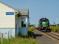 Leased GP38-2 1069 pulls a loaded ''Beluga'' train through disused Carleton VIA Rail station. These trains ran back and forth between Nouvelle and Maria in the summer of 2025, carrying crushed stones for the beach replenishment project in Maria. This project was handled by Construction Beluga, hence the train's nickname. On the tail end, leading the empty run that day was SFG 1849, the Amiral RS18u.