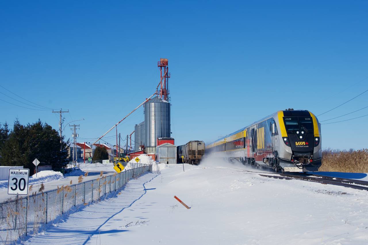 VIA 24 passes a maximum 30 kmh road sign as it flies by at probably about quadruple that speed. At left is a mill at Saint-Polycarpe that CN 589 will lift cars from a dozen minutes later.