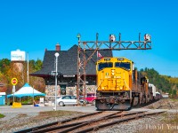 A large southbound freight rumbles past the historic station and under the old ABS cantilver signal bridge in downtown Temagami. Once a staple landmark, the old signal bridge finally came down in 2024 and the crossing got a face lift as well, outfitted with gates.