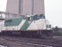 GO Transit 709 is seen with a commuter train west of Toronto Union Station in July of 1982. The concrete base of the giant CN Tower looms behind the GP40-2L 