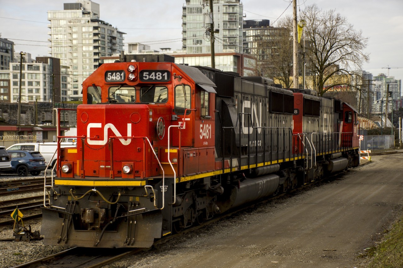 A pair of CN SD60s await their next job in the small CN New Westminster Yard. The locomotives look small compared to the modern high rise buildings in the background.