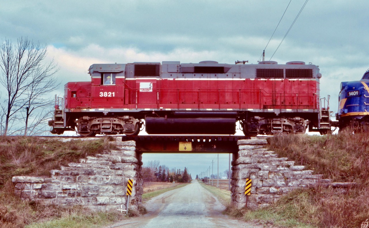 Bridging the gap. So much branchline railroading has vanished from Southern Ontario over the last few decades. It is nice to see, even today that the GEXR still has some nice rural trackage left, including some old photographic bridges. This shot was taken almost twenty years ago but most of the surviving trackage still looks the same. Unfortunately it’s hit and miss as far as catching a train. When the original GEXR started up in the early 1990’s many days you could still catch at least two trains running on its lines. Later that was lowered to basically one, and today, many days out of the week no train can be found along the rails west of Stratford. Here a typical consist for the time is slowly making its way over an old road bridge and through the rural countryside west of Stratford.