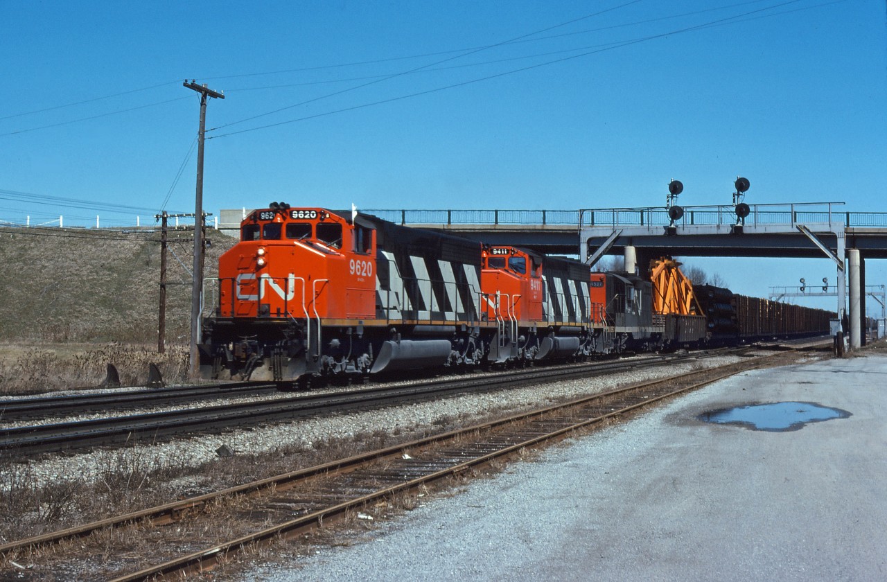 GP40-2LWs 9620 and 9411 along with GP9 4527 lead train 463, the "pulp train" (MacMillan Yard-Fort Erie), past Aldershot Yard and the Cold Storage building on a nice day in the spring of 1977. Note the dimensional load behind the power, where the crew can keep an eye on it.