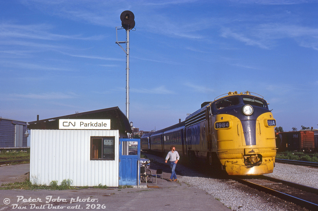 How the mighty have fallen: the once grand CN Parkdale Station has been replaced with this CN trainorder shack, at the junction with CN's Weston Sub and Newmarket Sub. Ontario Northland train #123, the "Northlander", is seen paused beside it waiting to head up the Newmarket Sub after departing downtown Toronto (timetables show #123 was due at Parkdale at 7:08pm, Friday & Sunday only). ONT FP7 1984 leads its TEE trainset consist. In the background is the upper portion of CP's own Parkdale Yard.

The original Parkdale Station was built in 1878 by the Northern Railway of Canada, and closed by CN in 1976. Facing demolition, a local station preservation group sprung up and got the station moved to Sunnyside, where it was unfortunately lost to fire by vagrants. Information on this replacement is scant - it's unclear how long this trainorder station shack or the operator based here lasted, possibly into the early-mid 1980's. Timetables mention it governed all movements to/from the Weston Sub to the Newmarket Sub. It looks like others have visited it in the past as well. Part of the CN freight shed on the left apparently became a fruit market in later years, and survived into the mid-2000's before demolition.

 Peter Jobe photo, Dan Dell'Unto collection slide.