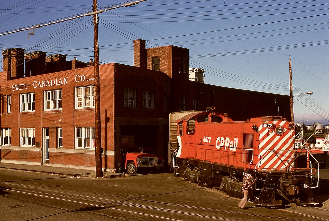 In Victoria, trackage continued past mileage 0.0 at the depot onto Store Street to reach a number of industrial customers, with Swift’s meat packing plant frequently a priority for the yard crew to switch with high-value loads.  On Saturday 1975-07-12, that was the case for MLW S-3 CP 6572 heading out of the spur at Swift Street to Store Street and onward to the Albion Yard distribution area.