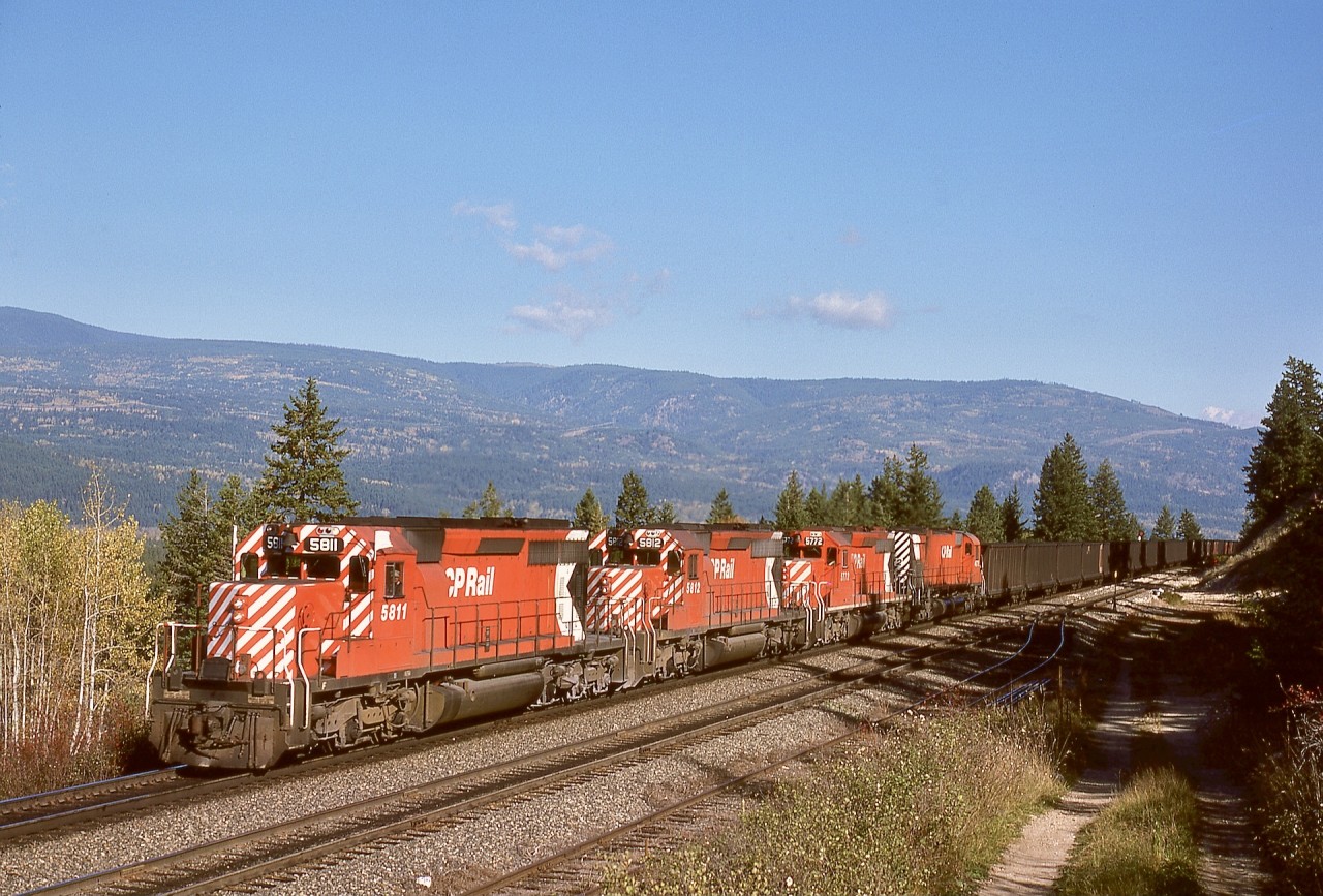 With dynamic brakes whirring, a loaded coal unit train from southeastern BC with CP 5811 + 5812 + 5772 + 4572 on the headend and unseen mid-train remotes 1017 + 5703 + 5642 + 5599 is descending from Notch Hill on the Shuswap sub. on Sunday 1976-10-17.  The era of exclusive MLW power on CP coal trains was long gone.