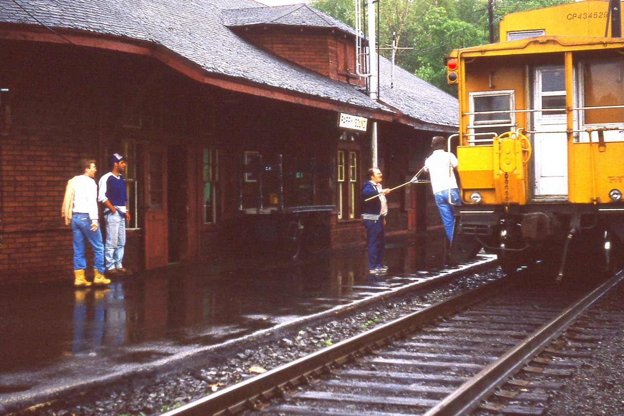 What a dismal dark day to be watching trains in Parry Sound. But, I'm there. Have to make the best of it. Even getting a decent setting with a film camera was difficult, which is obvious against this dark building.
Its been almost 40 years since this image and I have forgotten the name of the feller passing up the orders as this northbound train roars by.  Interesting old time scene.