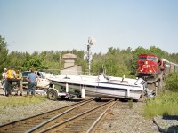 This was such an unusual incident.  I posted a photo more than 12 years ago of the train crews trying to push this boat off the track to no avail.  Figured this scene needed a revisit.
Luckily for all involved; a meet was to occur here, and the northbound train was just going into the siding and as a result the southbound pictured was moving rather slowly.
In this shot the boys are talking over what to do about this situation, (note the CP truck) and it turned out that all involved could not budge this boat, so the fork lift used by the boat storage place up on the hill came to the rescue.
I was just driving along and I heard the chatter on my scanner, which resulted in me showing up here. It appeared that, rolling over a very bumpy access road, the straps on the boat gave way and it slid off the trailer. I didn't ask questions.  My presence was not appreciated.
SB power in the photo  consists of a pair of SD90MAC, 9147 and 9153.  