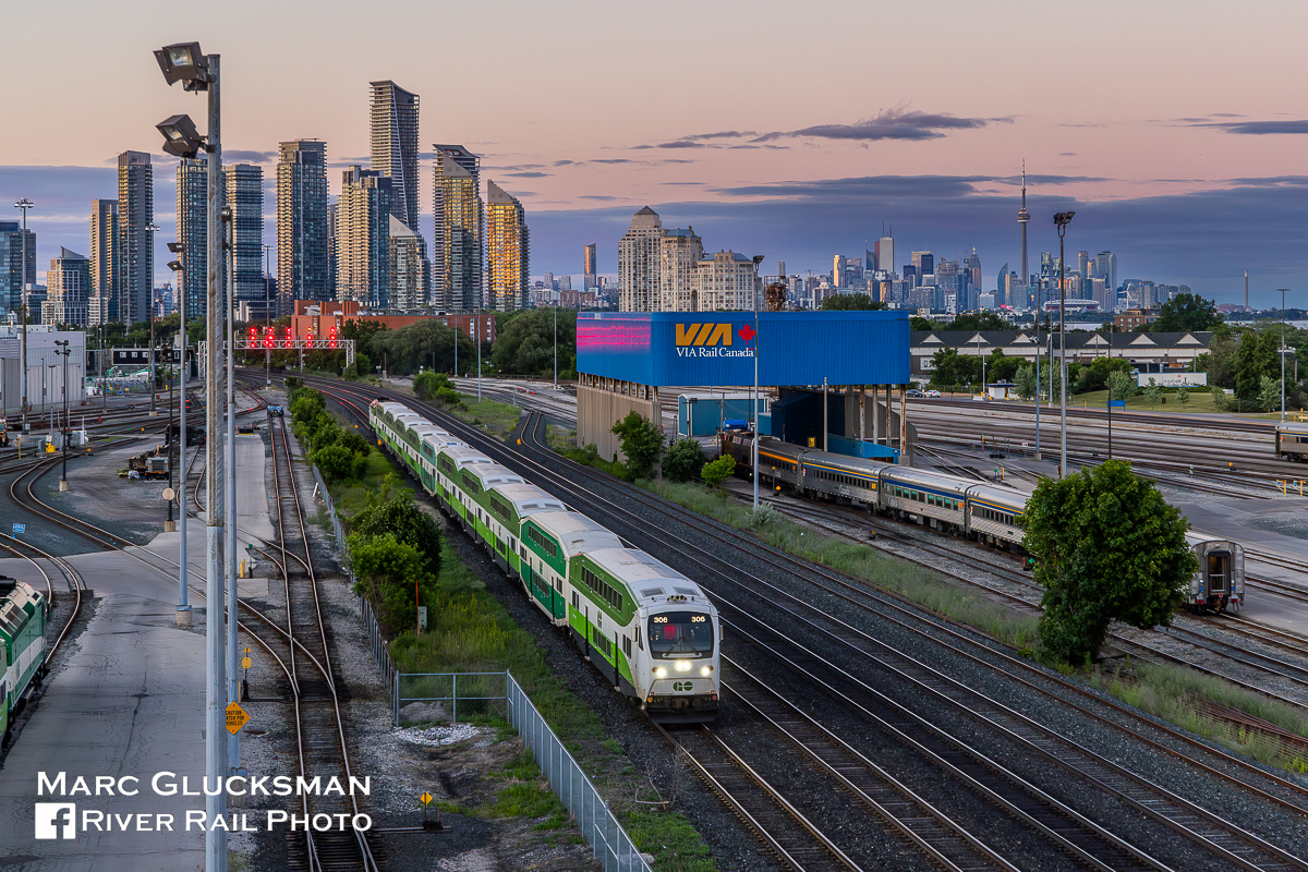 GO At Sunset. On the evening of June 27, 2022, GO Transit 306 (Bi-Level IX Cab Car, Bombardier) led a ten-car train by the yards near Islington Avenue in Toronto, Ontario. The Toronto Skyline is an attraction in and of itself, with the CN Tower keeping watch since 1976. The ten-car length is not uncommon; GO operates long consists to create high-capacity trains.