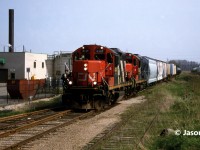 The CN 15:30 Kitchener Job is viewed arriving in Elmira, Ontario on the Waterloo Spur with a lengthy train and GP9RM’s 4141 and 7030. At the time, the job only operated with two units when it was necessary and on this day, both Nutrite and Sulco Chemicals in Elmira were receiving several cars. The springtime was always a busy time for Nutrite and their spur is seen to the right in the photo already full of hoppers previously set-off. 