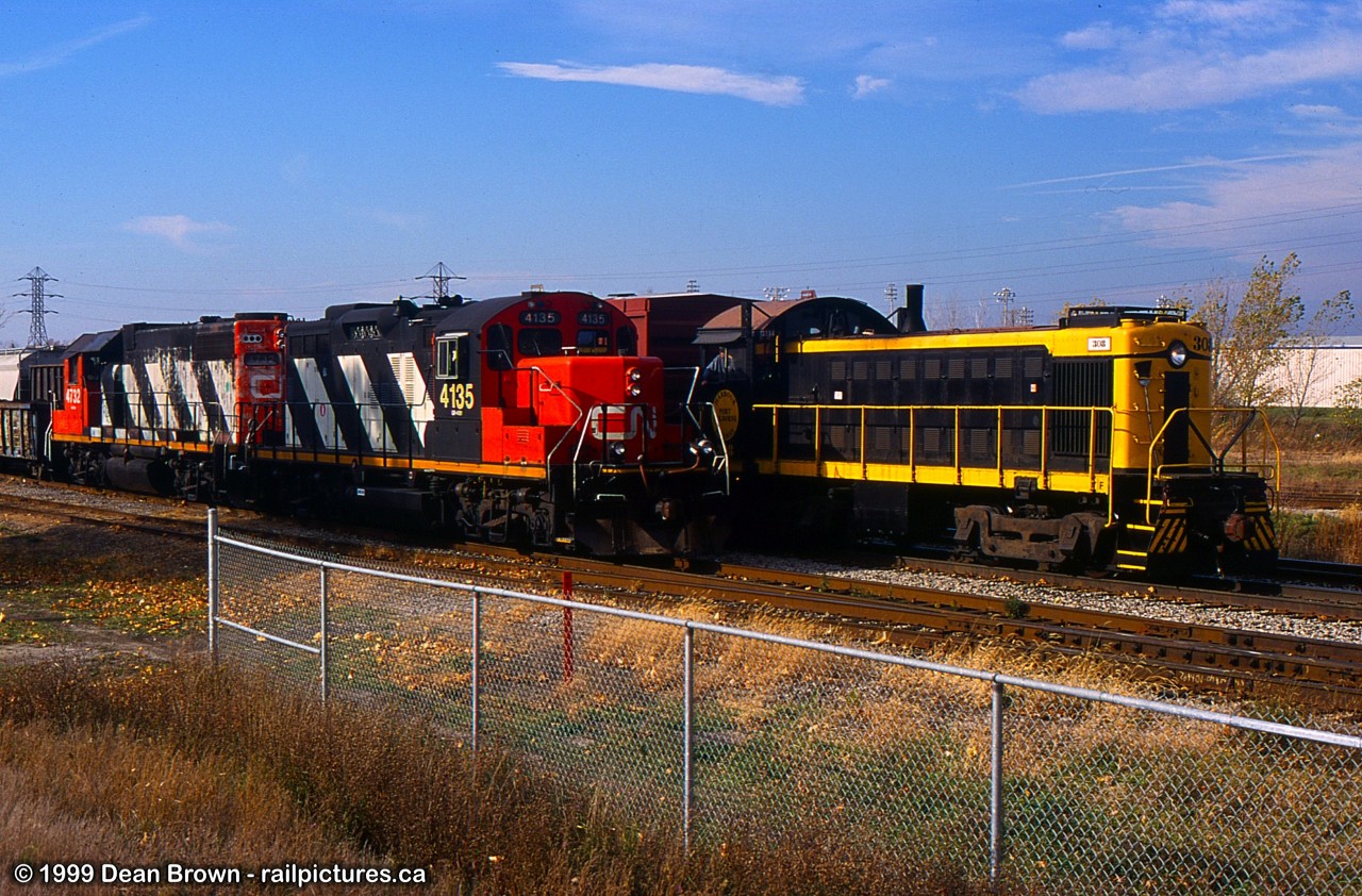 Merritton was a busy spot back in 1999 after Trillium Railway had taken over all the CN trackage in St. Catharines and Thorold. or CN ran 564 from Niagara Falls to Merritton to do the Interchange with Trillium for a short term. After a few weeks, the Interchange was transferred to Feeder. 

PCHR 308 waits for its cars on the south track of the CN Grimsby Sub while CN 564 is setting out and lifting cars on the south side.