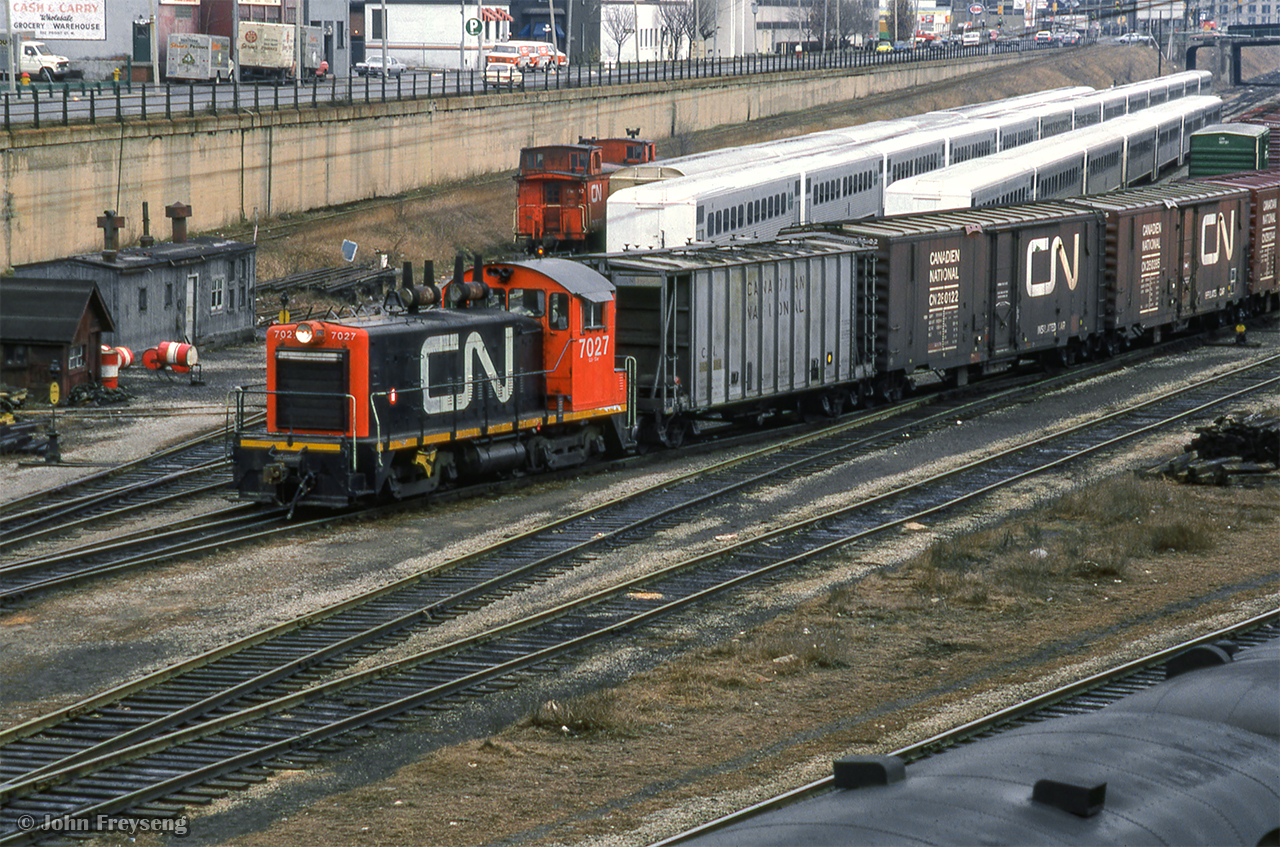 CN 7027 is seen working around Bathurst North Yard, passing an assortment of freight equipment and GO Transit single level cars.  The CPR spur along the south edge of Front Street can be seen, climbing to street level at Spadina Ave, and crossing north to their freight sheds at King Street (closed 1977) and a few small customers.  CNR's shed, located on the block south of CPR's, was accessed via a similar spur, just east of Spadina.

Scan and editing by Jacob Patterson.