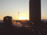 On what promises to be a nice September day, the sun rises on the westbound Super Continental  being serviced in Edmonton. Alas, in a little over two months, “the Super” will no longer call here—replaced by day trains between Winnipeg-Regina-Saskatoon, Saskatoon and Edmonton, as well as the “Rupert Rocket” extended to Edmonton. The passenger station was opened by Canadian National on 14 February 1966, and the CN Tower office building officially opened on 4 November 1966—at the time, the tallest office building in Western Canada.  Eighteen years after this photo was taken (on 3 September 1989), a restored Super Continental began the westbound pull-in/back-out move as CN phased out operations in downtown Edmonton. VIA would finally move to its current station near the Yellowhead Trail and Walker Yard on May 29, 1998. CN moved its office personnel out of the Tower a decade later. (Also note the heavyweight NAR passenger car next to the building.)