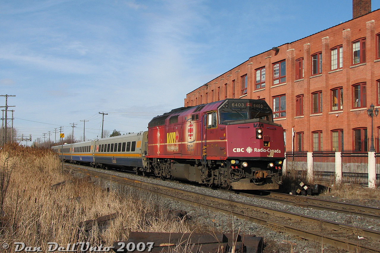 Outside of rush hour, time moved a little bit slower in downtown Brampton, allowing one time to stop and smell the trackside reeds in the ditch beside the tracks, people-watch some of the questionable individuals living in the old rental houses along Railroad Street, or just sit on the station platform passing the time, either awaiting the arrival of the afternoon VIA trains, or for Gusto's Pizza nearby to open for lunch (yum, lunch). Right now it's VIA time, with #84 putting in its daily appearance downtown on its way to downtown Toronto. VIA F40PH-2D 6403 leads the consist today, wrapped in its unique purple-red livery for CBC's 50th anniversary. The trailing LRC cars are just finishing clattering over the diamond before the train crosses Mill Street and makes its station stop.

Normally we'd wait for VIA #85 to show up too, but we only had enough time for #84 before the afternoon GO bus ride to downtown Toronto beckoned us to the bus terminal nearby (often also populated by questionable individuals, some of whom were known to have been retailers, of a sort, for questionable substances. Partaking in such if offered was not recommended).