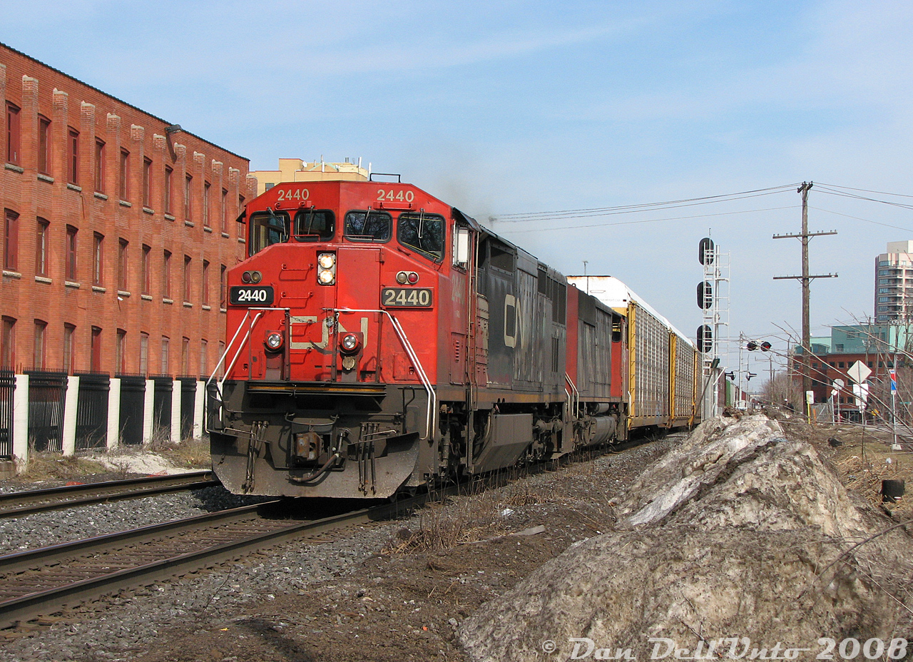 A pair of back-to-back "Draper Taper" cowl units, CN C40-8M 2440 and SD50F 5434, lead afternoon train #393 westbound through downtown Brampton. They've just past the VIA/GO Brampton Station and Mill Street crossing, and are about to slam the CN-OBRY Brampton diamond just out of frame next to the photographer. Some absolutely filthy snow, piled here by the snowplow contractor in charge of clearing the south GO parking lot, sticks around as a blight on the landscape a bit longer.