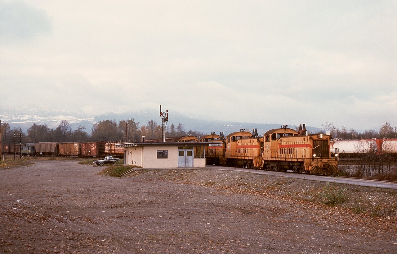 Due to its regular route from New Westminster to Huntingdon unavailable due to bridge work, the BC Hydro eastward Valley Freight detoured over Canadian Pacific lines (Westminster, Cascade, and Mission subdivisions) on Monday 1975-11-17, and due to six-axle units forbidden on CP at Sapperton near New Westminster, four SW900s, BCH 907 + 902 + 906 + 910, powered that train, and it is shown here at CP’s Coquitlam depot and train order office JN (from Junction, versus YD in the yard office control tower in the yard) at 1500 PST.

Years later, that depot in Port Coquitlam was renamed Port Coquitlam to minimize confusion for Westcoast Express commuter train passengers, and that area is now an extensive commuter rail and transit bus depot.