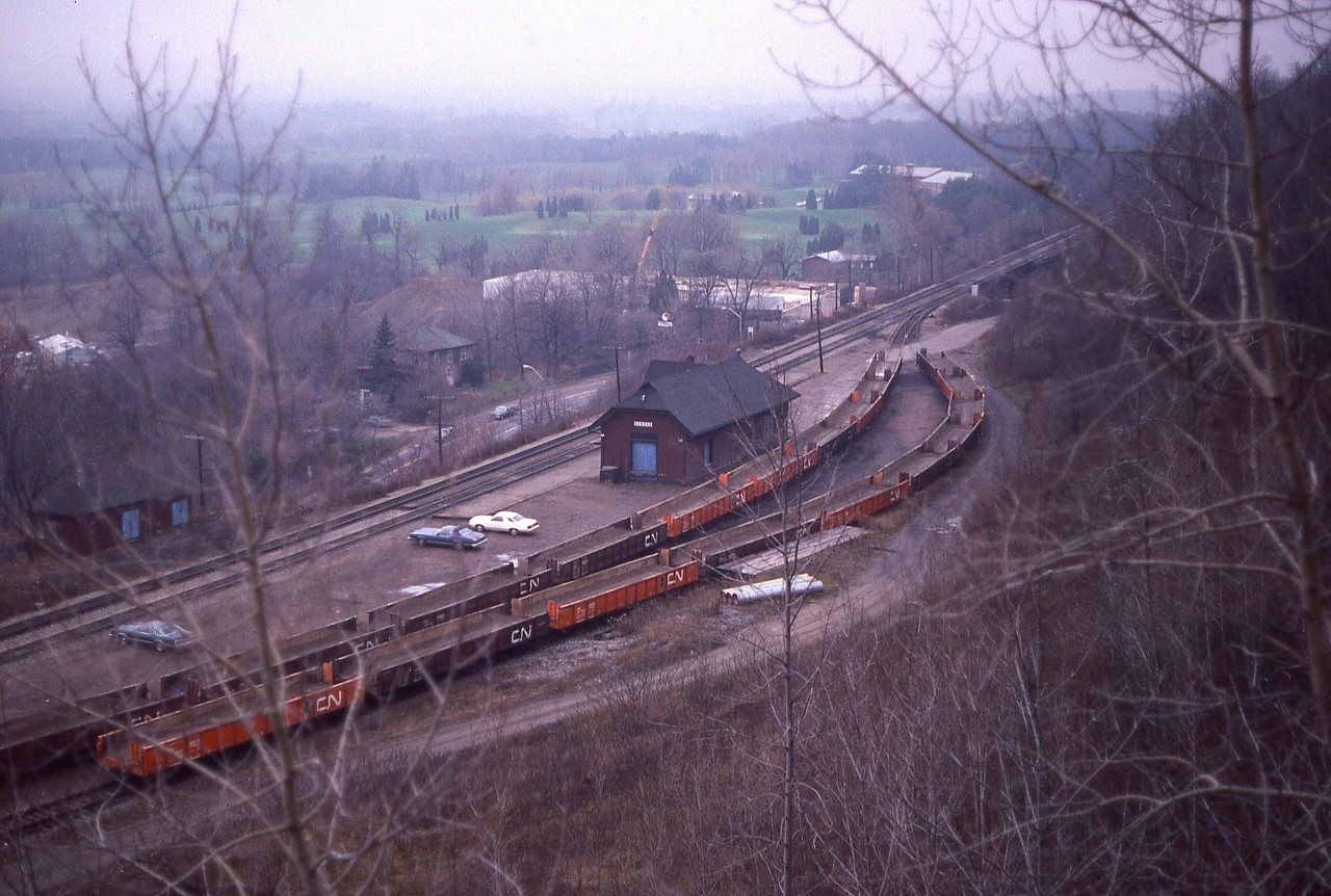 An overview of the old Dundas station. I don't know what possessed me to try 'mountain goat' antics by wandering thru the brush of the hillside above the station area, but it did present a decent view of the station and surrounding area. In the foreground notably are two columns of 48 ft mill gondolas converted to OCS service that  go with Pettibone Speed Loader machines. Note opposing drop aprons on each car, which enables continuous rip-rap unloading by those old rubber tired vehicles(now history). The cars were used mostly in construction areas, such as siding extensions for shoring up weakened areas along the right of way. No, I did not turn scholar; this information on the gons is courtesy of Paul O'Shell. (any errors are mine)
The station, as most fans know; suffered from a fire and eventually was demolished.