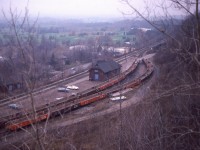 An overview of the old Dundas station. I don't know what possessed me to try 'mountain goat' antics by wandering thru the brush of the hillside above the station area, but it did present a decent view of the station and surrounding area. In the foreground notably are two columns of 48 ft mill gondolas converted to OCS service that  go with Pettibone Speed Loader machines. Note opposing drop aprons on each car, which enables continuous rip-rap unloading by those old rubber tired vehicles(now history). The cars were used mostly in construction areas, such as siding extensions for shoring up weakened areas along the right of way. No, I did not turn scholar; this information on the gons is courtesy of Paul O'Shell. (any errors are mine)
The station, as most fans know; suffered from a fire and eventually was demolished.
