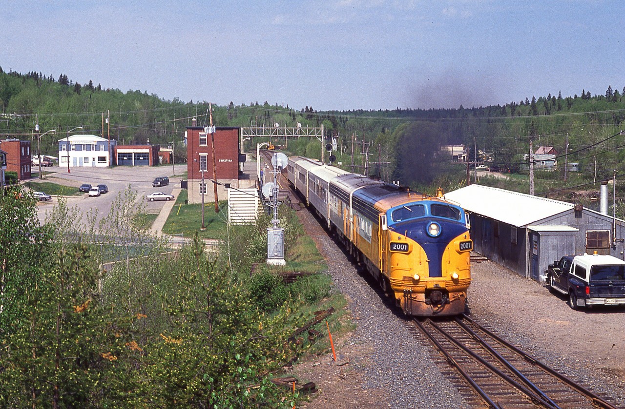 A beautiful June morning sees the southbound Northlander with ONR 2001 pulling away from a stop at the Swastika 'station' in this wide-angle view that shows most of the communities downtown area. Second unit is auxiliary power unit #205.
I'm standing on a makeshift platform of boards against a pine tree in order to get some elevation.
It will be nice to see the rebirth of the ONR Northlander. I just wish it would be a daylight run.