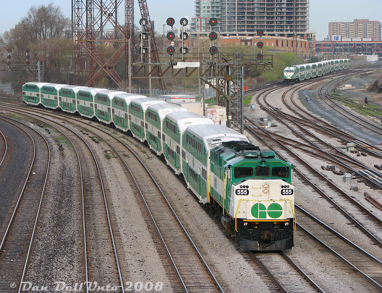 Every excellent morning starts bright and early with a good night's sleep, an uneventful train ride in, and a brisk walk from Union Station all the way to Bathurst Street to shoot a gazillion GO F59PH units handling the morning rush hour traffic. One of many seen that morning, GO Transit "Triple Nickel" 555, cruises into the Union Station Rail Corridor on eastbound Lakeshore line train #452, while in the distance, brand new MP40PH-3C 605 is snaking through the crossovers at Strachan Avenue on Milton line train #152. 

The few newly active MP40 units at the time would be regularly assigned to Milton line trains, enabling GO to run longer 12 car consists to make up for the lack of track time CP allowed to run extra trains. The limiting factor on F59PH units like 555 was the HEP, which could only provide power for a maximum of 10 bilevels.

GO 555 would be made surplus by the second flood of new MP40 deliveries, a fairer unit in GO's eyes, and unlovingly shed with 9 other F59 siblings to AMT/exo in 2011 (renumbered as AMT 1348). GO would court and woo back the favour of 555 and three other units in 2026 for their future "F59 Renaissance" period, bestowing her the new number of GOTX 580 (restoring her to her former glory as 555 however, would be a much fairer number of prestige to bestow upon one so unwillingly cast off, only to be swept back close to Metrolinx's bosom in their time of need).