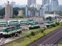 2008 for GO Transit was the beginning of the end of the F59PH fleet: as new MP40PH-3C units from MPI started to come online, old F59's started to populate the deadlines around Willowbrook Yard. Some were just stored out of service, while others had pushed their last bilevel. Units from the first order (520-535, built 1988) were the first to go: stored here are 531, 541 and 556 elephant style, the pair 532 and 520 back-to-back at the bumper, and 524, 533 and 521 shoved out of the way at the far end. It was very rare to see a unit facing west, but GO turned one or two units to serve as shop switchers around Willowbrook in their later years (a back-to-back pair even made it out in revenue service). Two employees work on the closest units under blue flag protection, perhaps assessing 533's condition for potential sale. 541 and 556 would return back to work for a year or two, but the rest sold between March-May 2009 as the <a href=http://www.railpictures.ca/?attachment_id=16385><b>deadlines grew more</b></a>. Unit 563, still active, is pictured in the background getting ready to take out a PM rush hour train.<br><br>Other neat things in this photo are the low building behind the sound barrier wall belonging to Canadian Foundry Supplies (now demolished, they had their own siding that received hoppers into at least 2007). In the distance on the right is GO's Mimico station, and all the condos in the distance along the Lake Shore repopulated the old motel strip. If you eye-spy a bit, you can pick out the water tower for <a href=http://www.railpictures.ca/?attachment_id=47105><b>Mr. Christie's Lakeshore Bakery</b></a> (still active, later demolished), and the blue load-test unit built from an EMD dynamic brake hatch. And on this day, brand new MP40's 600, 626 and 614 were sitting at the west end of the shops (out of view) newly delivered and awaiting preparations for service.