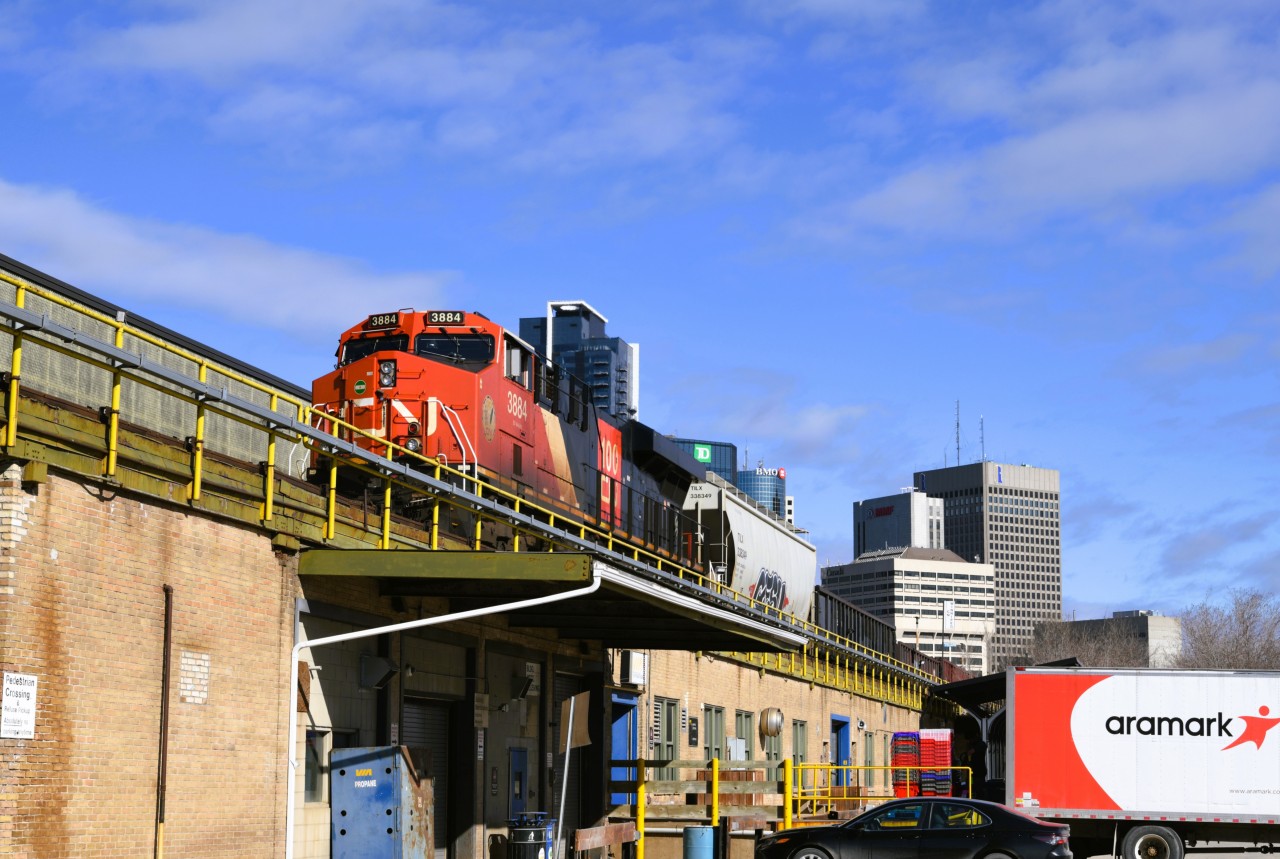 Look up, Look way up  
CN 3884 leading a mixed freight consist stalled as it was making its way past the elevated Winnipeg train shed causing a delay in departure of VIA 693 my Winnipeg to Churchill train. 
While anxious to get on board and start the journey, this delay allowed for a little more outdoor photo time as well as a delicious lunch at Fergie's Fish & Chips in the refurbished ex-CN Express Garage building at The Forks Market behind VIA Rail's Union Station. 
Below the stalled freight is VIA Rail's shipping & receiving dock and warehouse.