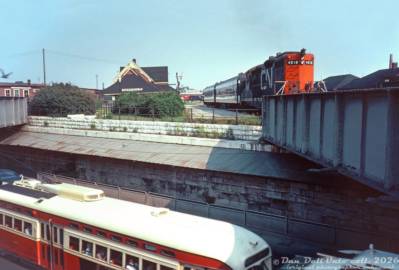 A rather unconventional angle of Parkdale, with a few photographic faux-paux, but full of all sorts of rich content: CN GP9 4518 (a freight unit) pulling today's "Barrie Bullet" commuter train for the Newmarket Sub, is seen making its station stop at CN's Parkdale Station (replaced with a CN insta-shack a few years later). To the left is CN's old Parkdale freight shed. To the upper right is the roof of CP's own Parkdale Station building (closed a few years earlier in 1968) and yards visible in the distance. The main CN Weston Sub crossed the steel girder bridge on the right, the one on the left had a service track running north to CN's small yard and facilities nearby.

Below, traffic passes by on the busy Queen Street West, including TTC PCC streetcar 4485 on the Queen route. On the left site along the brick retaining wall under the awning, one can see the opening and stairway that led up from Queen Street to CN's Parkdale Station above (there was a similar stairway to access CP's Parkdale Station off Dufferin Street).

This neat photo was taken by the same unknown Toronto-area photographer who took this shot of GO 9807 from a slightly different angle, on the same day, in the same spot.

Original photographer unknown, Dan Dell'Unto collection slide.