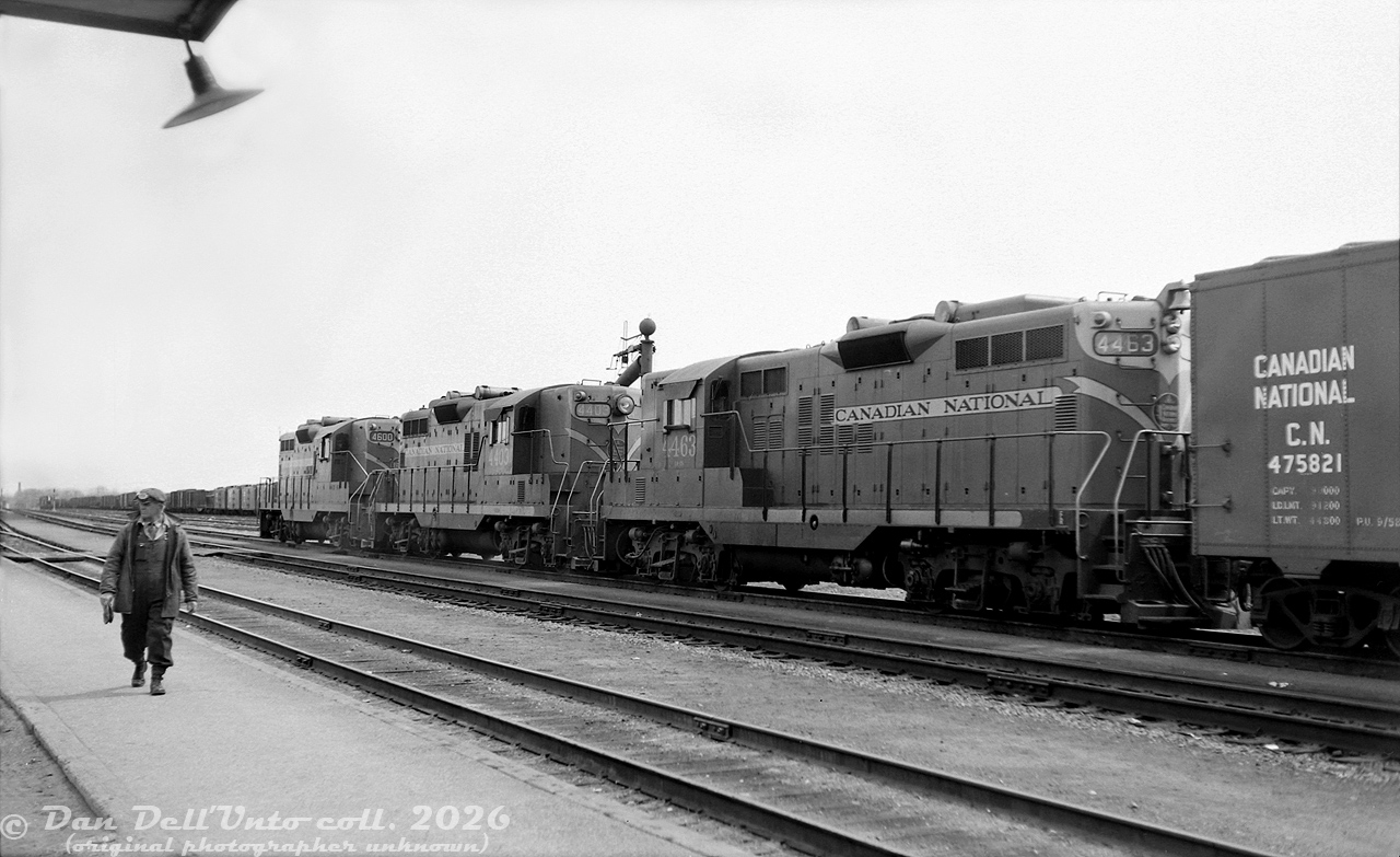 Three of CN's plentiful GP9 units, 4463, 4403 and 4600, sit in front of the station at Danforth in east-end Toronto on an eastbound freight, as a member of the crew walks the platform, appearing to be eyeing the station. It's April 1961, and the last steam engines on the system had just been retired the previous year in favour of hoards of first-generation diesels such as GMD's popular GP9 model. Notes by the unknown photographer of this negative indicate the train was of ample size at 103 cars long, would likely would have required a helper engine for the eastbound grade here in the steam era. Freight cars visible in the background are parked in the adjacent Danforth Yard, CN's main east-end Toronto freight yard that would hold importance until its gradual decline after the "Toronto Bypass" and Toronto (MacMillan) Yard opened to the north of the city. Today the yard has been redeveloped into housing, and this location is now home to Danforth GO Station.

For the modelers out there, CN's 44/45/4600-series GP9's were regular or "heavy" freight units, as opposed to the light-weight 41/42/4300-series units. 4403 is one of the earliest such GP9's, exhibiting the old Pyle reflector style or "ash can" barrel headlights, a Phase 1 carbody configuration and early bolted stanchions. The other two units are later Phase 2 GP9's, but feature a unique-to-CN carbody louvre arrangement that moved one of the 2x3 set onto the next door, in order to spell out the full "Canadian National" lettering clearly. These units all had smaller 1000 gallon (imperial) fuel tanks, versus the more common 1333 gallon (imp, or 1600 US gallons) found on other railways. Rooftop-mounted spark arrestors and a long hood mounted bell are typical CN fare. In a way it's fitting that similar-looking CN GP7 4803 is preserved at the Toronto Railway Museum, a good representation of all the early CN Geeps that once handled freight in the post-dieselization era.

Original photographer unknown, Dan Dell'Unto collection negative.
